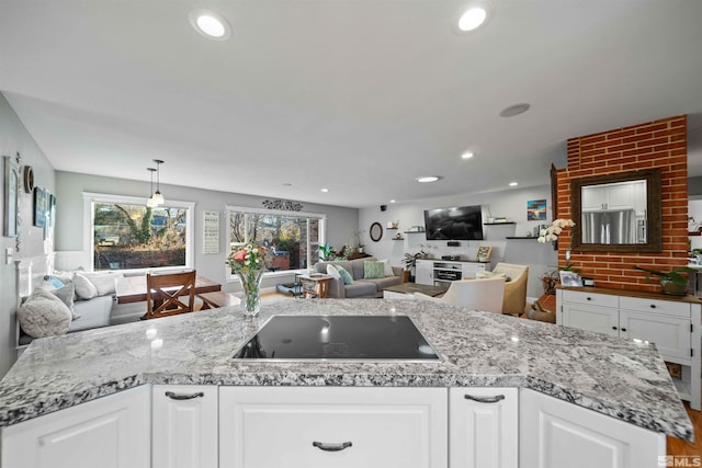 kitchen with white cabinetry, an island with sink, black electric stovetop, light stone countertops, and pendant lighting