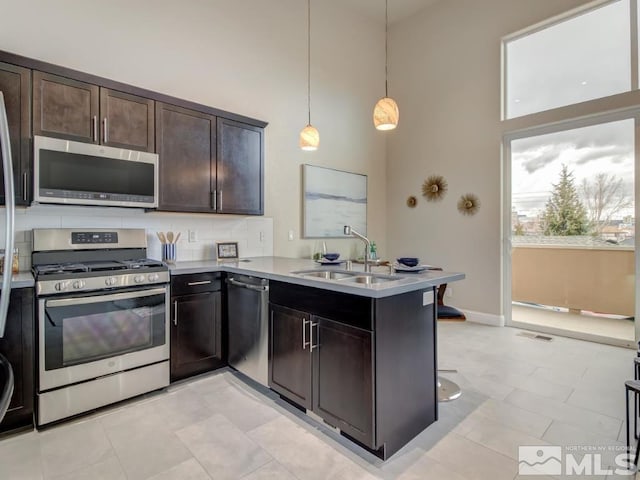 kitchen featuring decorative light fixtures, kitchen peninsula, sink, a high ceiling, and appliances with stainless steel finishes