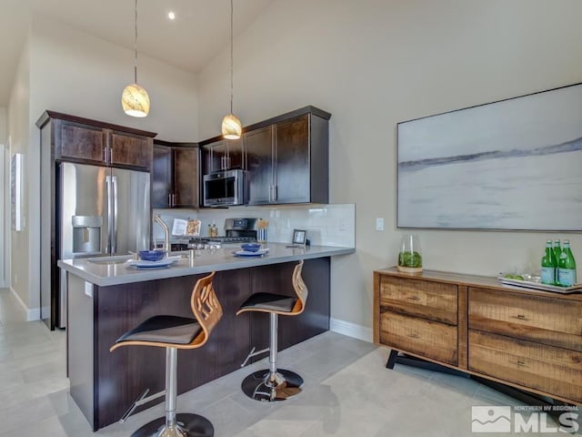 kitchen with appliances with stainless steel finishes, a kitchen breakfast bar, hanging light fixtures, kitchen peninsula, and high vaulted ceiling