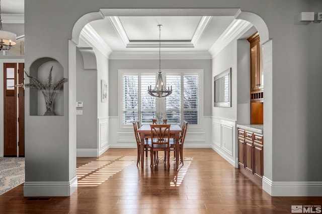 dining room with a raised ceiling, dark hardwood / wood-style flooring, crown molding, and a chandelier