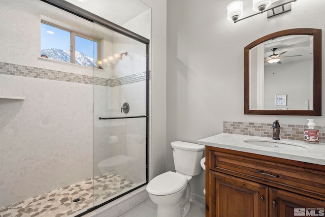 bathroom featuring toilet, a shower with shower door, ceiling fan, backsplash, and vanity