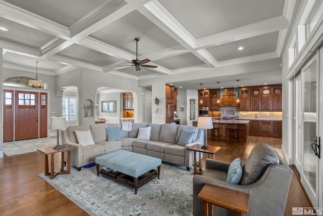 living room featuring dark hardwood / wood-style floors, beamed ceiling, crown molding, coffered ceiling, and ceiling fan with notable chandelier