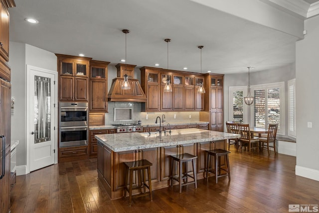 kitchen featuring decorative light fixtures, stainless steel appliances, an island with sink, tasteful backsplash, and sink