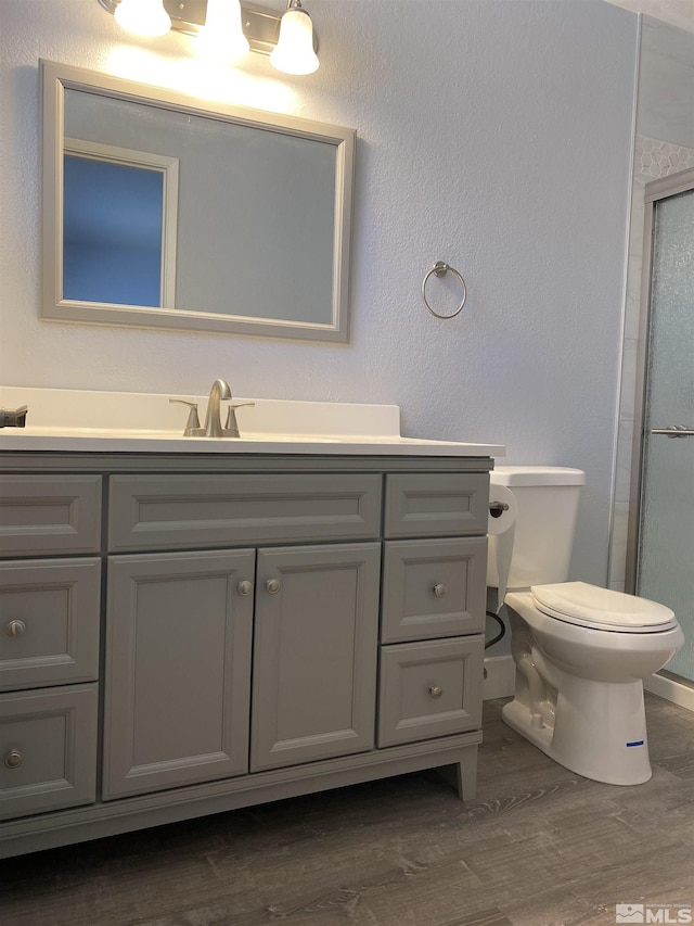 bathroom with walk in shower, vanity, wood-type flooring, and toilet