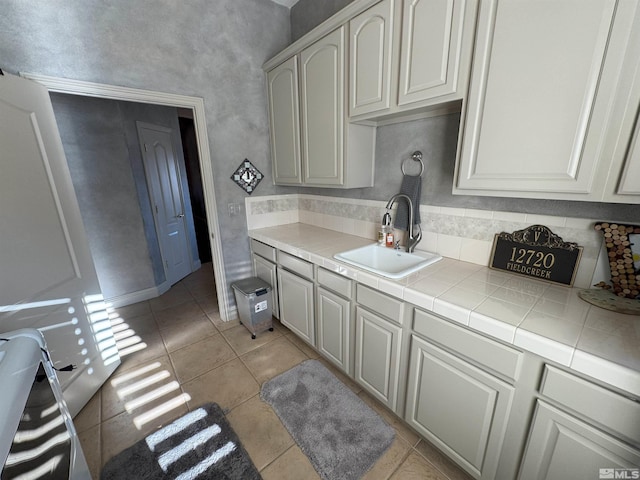 kitchen featuring tile counters, light tile patterned floors, sink, and white cabinetry