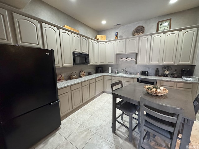 kitchen featuring light stone countertops, sink, light tile patterned floors, and black appliances