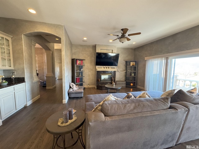 living room featuring decorative columns, dark wood-type flooring, ceiling fan, and a fireplace