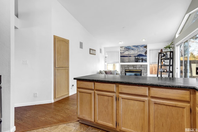 kitchen featuring light brown cabinetry, light tile patterned floors, lofted ceiling, and a fireplace