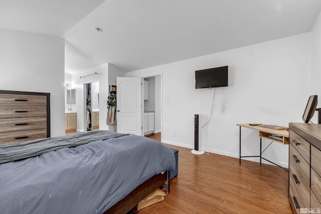 bedroom with vaulted ceiling, wood-type flooring, and ensuite bath