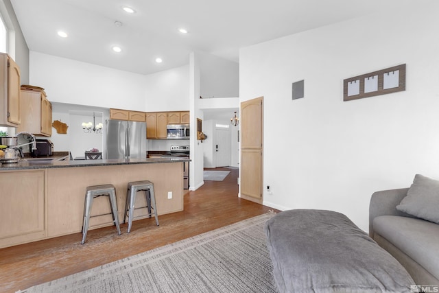 kitchen featuring kitchen peninsula, a towering ceiling, hanging light fixtures, light wood-type flooring, and appliances with stainless steel finishes