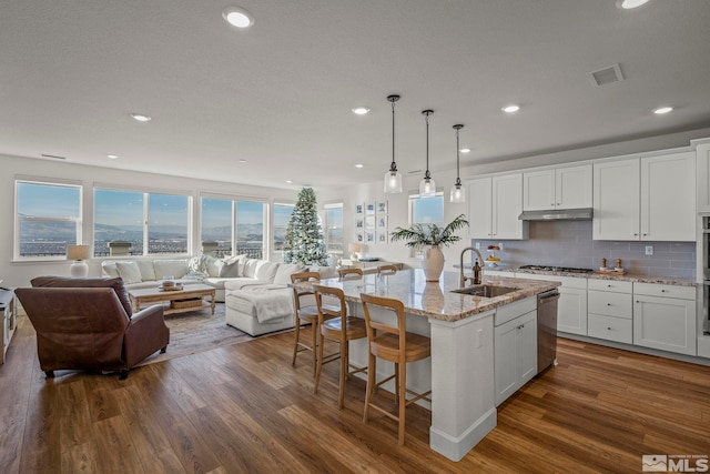 kitchen with decorative light fixtures, sink, a kitchen island with sink, white cabinets, and light stone counters