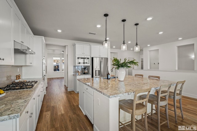 kitchen featuring decorative light fixtures, appliances with stainless steel finishes, an island with sink, a kitchen breakfast bar, and white cabinets