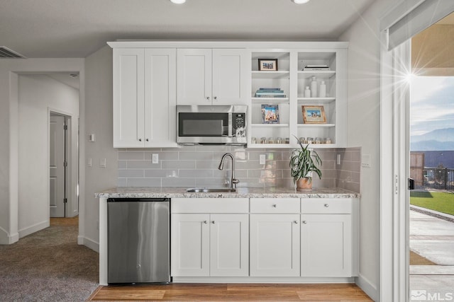 kitchen featuring light stone countertops, sink, light colored carpet, and white cabinets