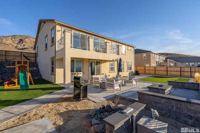 back of property with a yard, an outdoor living space with a fire pit, a patio, and a playground