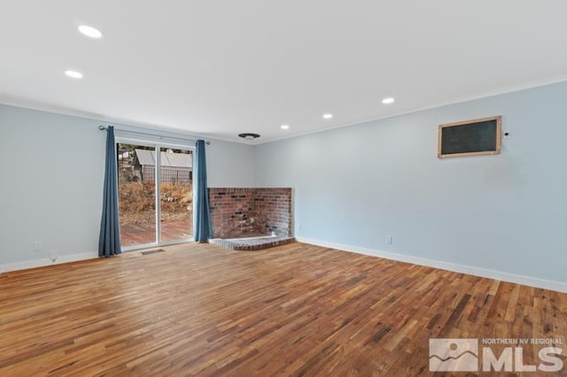 unfurnished living room with wood-type flooring, a brick fireplace, and ornamental molding