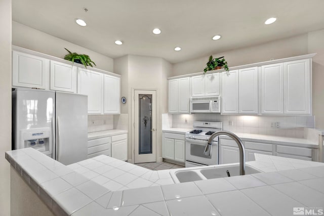 kitchen featuring backsplash, tile countertops, sink, white appliances, and white cabinetry