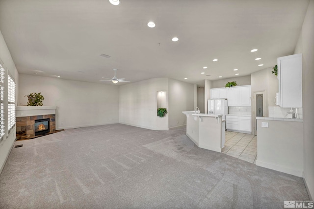 unfurnished living room featuring ceiling fan, light colored carpet, and a tiled fireplace