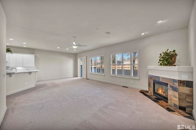 unfurnished living room with ceiling fan, light colored carpet, and a tiled fireplace