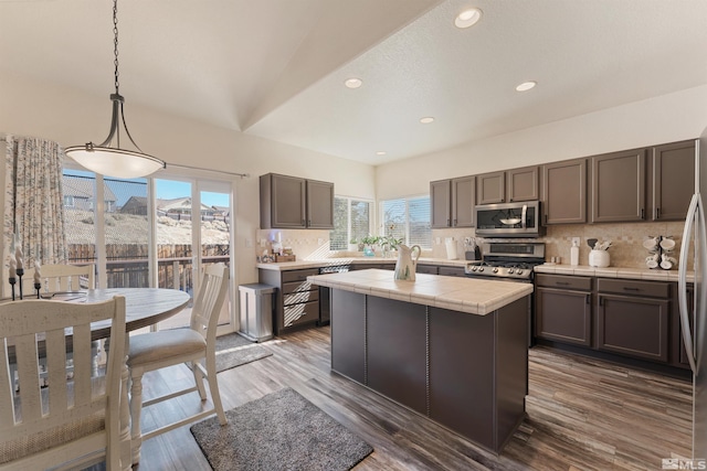 kitchen with stainless steel appliances, tasteful backsplash, decorative light fixtures, dark hardwood / wood-style flooring, and a kitchen island