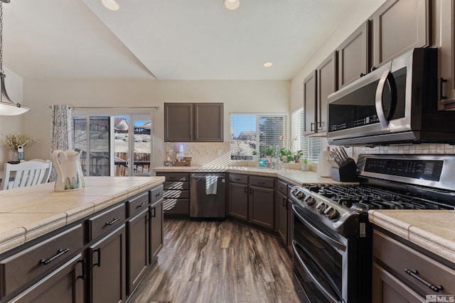 kitchen featuring tile countertops, stainless steel appliances, dark wood-type flooring, pendant lighting, and dark brown cabinetry