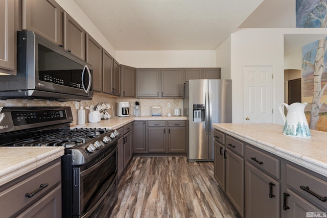 kitchen featuring backsplash, dark wood-type flooring, tile countertops, and stainless steel appliances