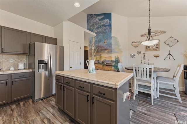 kitchen featuring stainless steel refrigerator with ice dispenser, tasteful backsplash, dark wood-type flooring, hanging light fixtures, and a center island