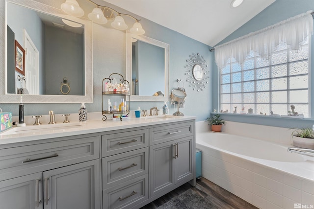 bathroom featuring hardwood / wood-style flooring, a relaxing tiled tub, vanity, and vaulted ceiling