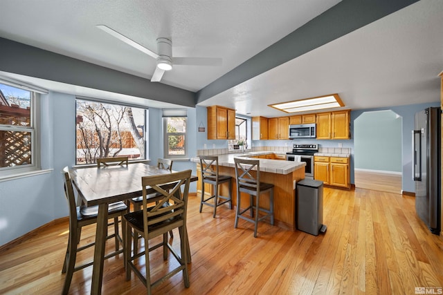 kitchen featuring a breakfast bar area, light wood-type flooring, stainless steel appliances, and ceiling fan