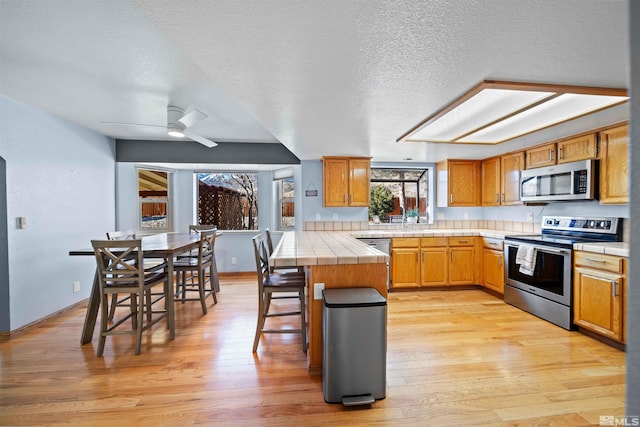 kitchen with ceiling fan, light hardwood / wood-style floors, a breakfast bar, stainless steel appliances, and tile counters