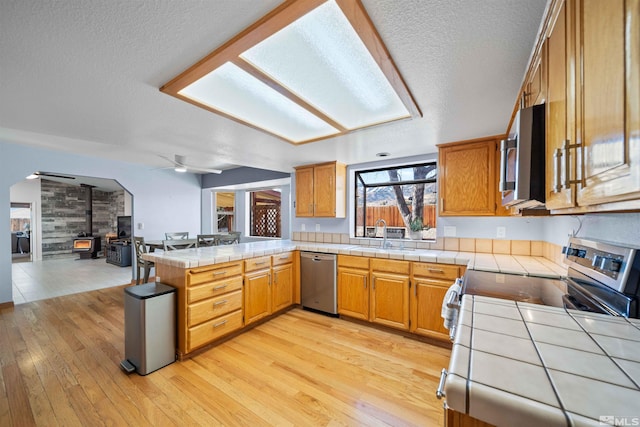 kitchen featuring appliances with stainless steel finishes, tile counters, light hardwood / wood-style floors, sink, and a wood stove