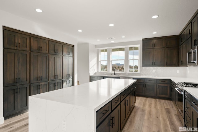 kitchen with stainless steel appliances, light hardwood / wood-style floors, dark brown cabinetry, and a center island