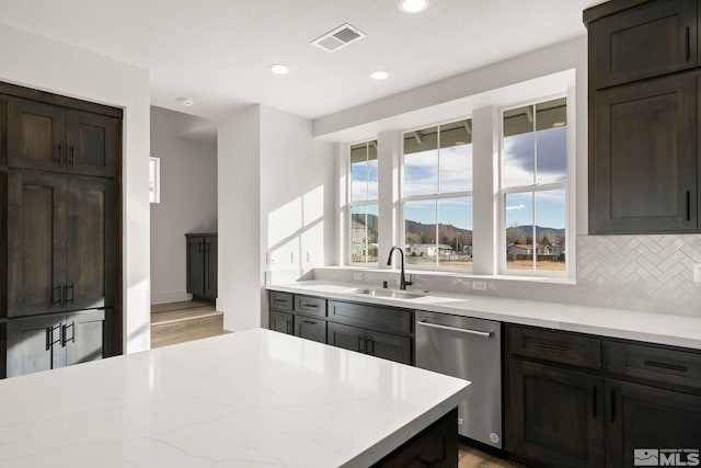 kitchen featuring decorative backsplash, dark brown cabinets, stainless steel dishwasher, light stone counters, and sink