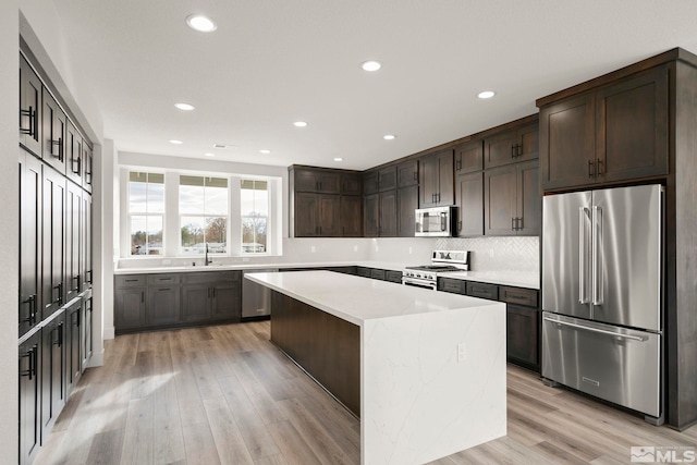 kitchen with light hardwood / wood-style floors, premium appliances, dark brown cabinetry, and a center island