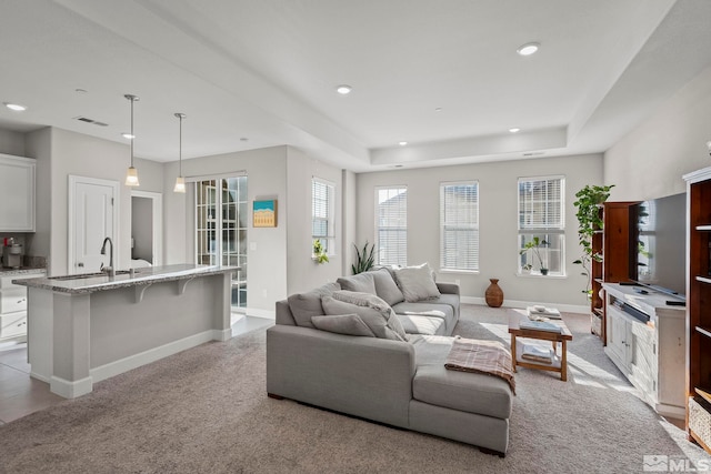 carpeted living room featuring a raised ceiling and sink