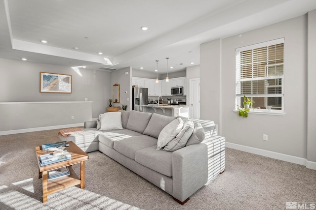 living room with light colored carpet, a raised ceiling, and sink