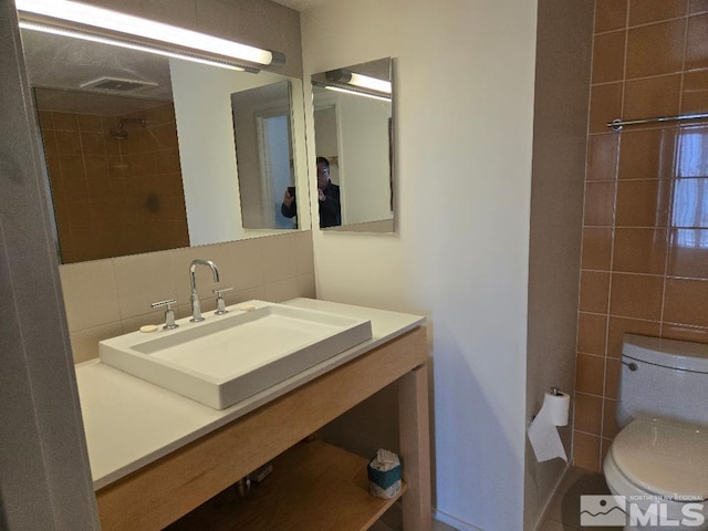 bathroom featuring sink, backsplash, toilet, and tile walls