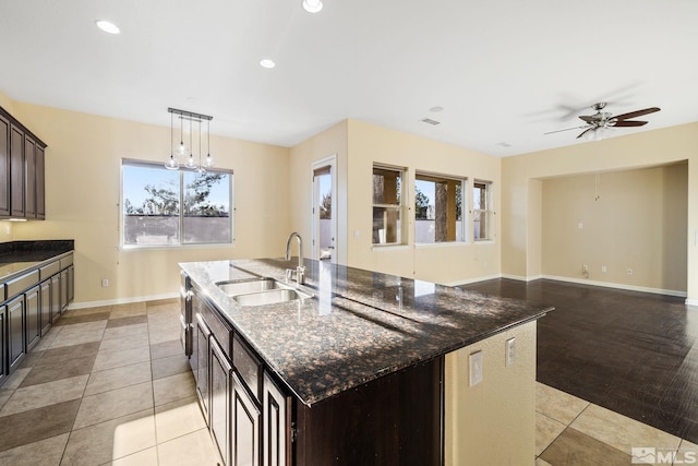 kitchen featuring an island with sink, sink, hanging light fixtures, ceiling fan, and dark brown cabinets