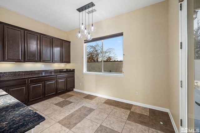 kitchen featuring decorative light fixtures, a notable chandelier, dark stone countertops, light tile patterned floors, and dark brown cabinets