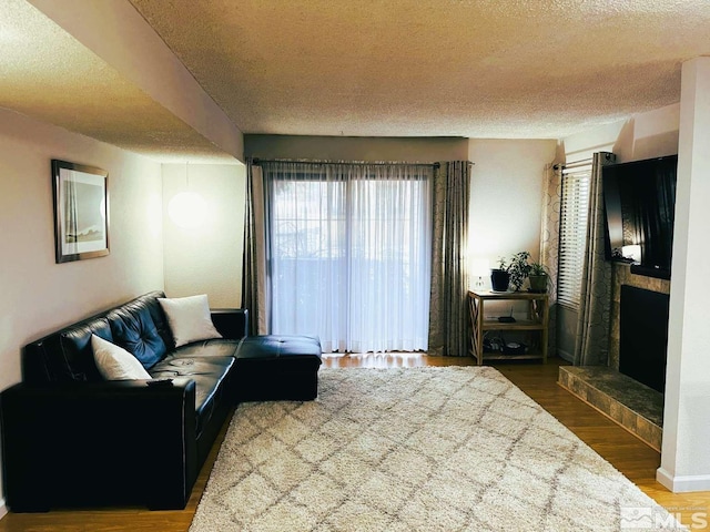 living room with a textured ceiling, dark wood-type flooring, plenty of natural light, and a tiled fireplace