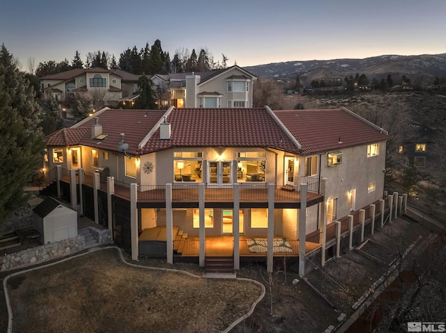 back house at dusk with a deck with mountain view and a storage unit