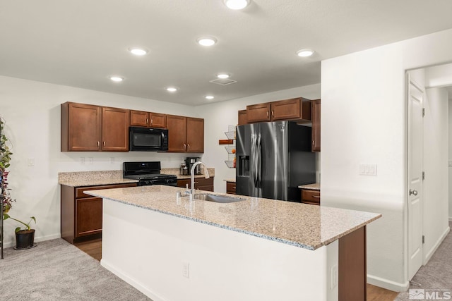 kitchen featuring black appliances, carpet floors, an island with sink, sink, and light stone counters