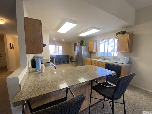 kitchen featuring dishwasher, kitchen peninsula, a kitchen bar, sink, and stainless steel fridge