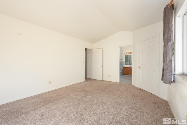 unfurnished bedroom featuring connected bathroom, light carpet, and vaulted ceiling