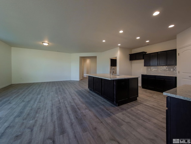 kitchen with sink, wood-type flooring, tasteful backsplash, and a kitchen island with sink