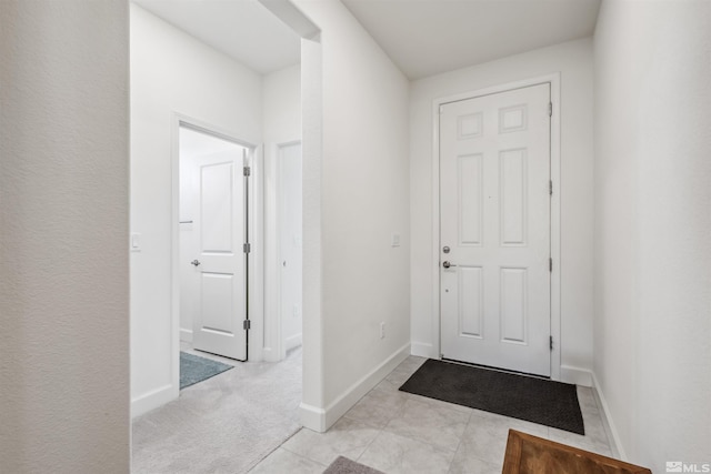 entryway featuring light tile patterned floors, baseboards, and light colored carpet