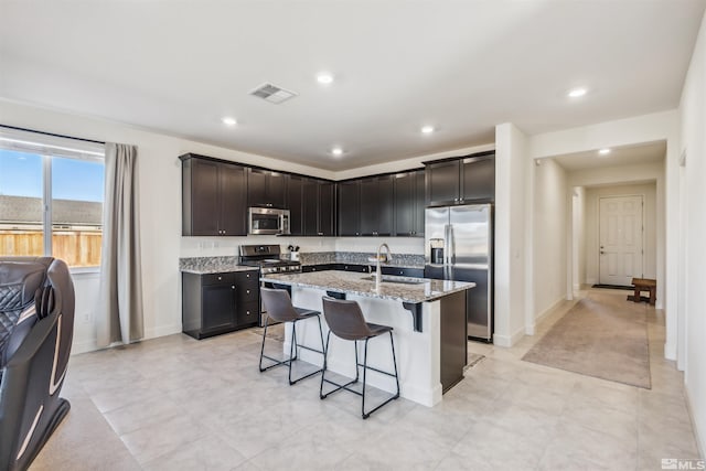 kitchen with light stone counters, stainless steel appliances, visible vents, a sink, and a kitchen breakfast bar