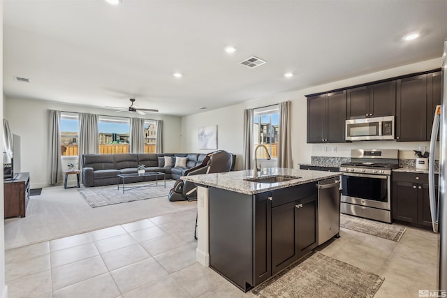 kitchen with visible vents, an island with sink, light stone countertops, stainless steel appliances, and a sink