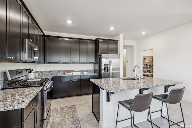 kitchen featuring stainless steel appliances, light stone counters, a kitchen bar, and a sink