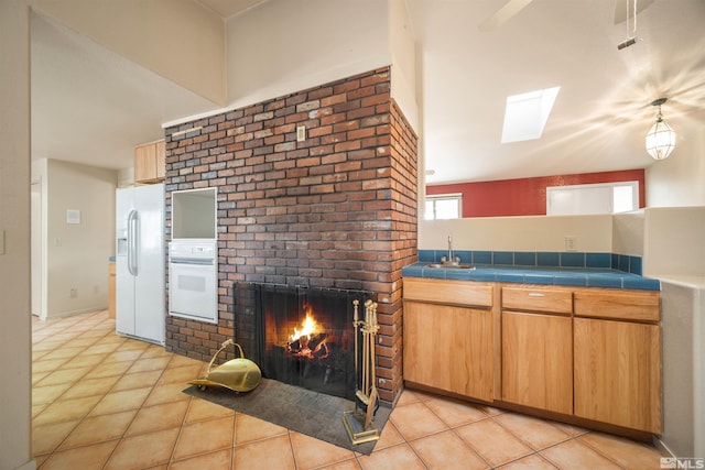 kitchen with a fireplace, tile countertops, sink, white appliances, and light tile patterned floors