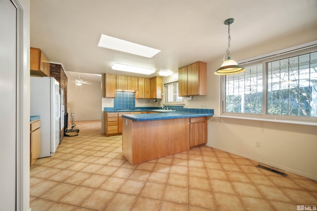 kitchen with ceiling fan, white fridge, kitchen peninsula, sink, and a skylight